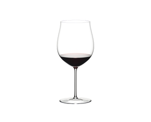 A hand holds a RIEDEL Amadeo Decanter and pours red wine into a RIEDEL Sommeliers Burgundy Grand Cru glass, which stands on a light grey ground.