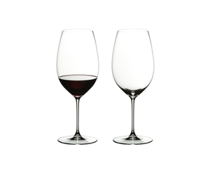 Two RIEDEL Veritas New World Shiraz glasses side by side. The glass standing on the left side is filled with red wine, the other one is empty.