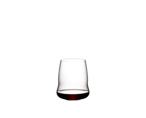 A woman is holding a SL RIEDEL Stemless Wings Cabernet/Merlot glass filled with red wine. The glass is in focus and the background is blurry.