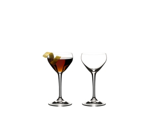 Two RIEDEL Drink Specific Glassware Nick & Nora glasses one filled with a brown drink and one unfilled on a white background.