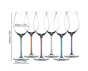 Six RIEDEL Fatto A Mano Champagne Wine Glasses with different coloured stems (f.l.t.r.: mint, orange, mauve, white, turquoise and violet) stand around an open champagne bottle on a light grey ground against a light grey background.