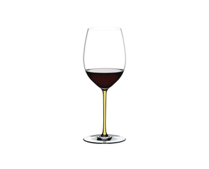 A RIEDEL Fatto A Mano Cabernet/Merlot glass in yellow filled with red wine on a transparent background. 