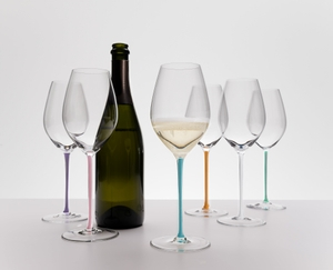 6 champagne filled RIEDEL Fatto A Mano Champagne Wine Glasses with stems which are colored in mint, orange, mauve, white, turquoise and violet stand slightly offset side by side on white background.