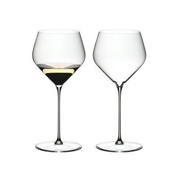 Two RIEDEL Veloce Chardonnay glasses one filled with white wine and one unfilled on a white background.