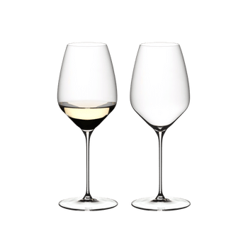 Two RIEDEL Veloce Riesling glasses one filled with white wine and an unfilled glass on a white background.