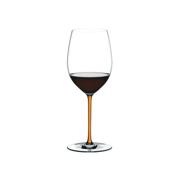 A RIEDEL Fatto A Mano Cabernet with an orange stem and filled with red wine.