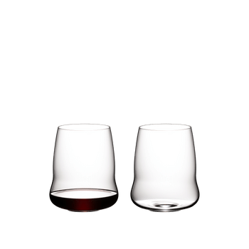 Two SL RIEDEL Stemless Wings Cabernet/Merlot glasses on a white background. The SL RIEDEL Stemless Wings Cabernet/Merlot glass on the left side is filled with red wine, the other one is unfilled.