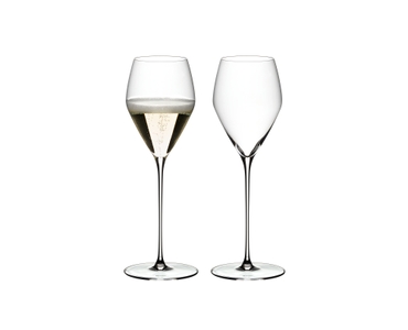 Two RIEDEL Veloce Champagne Wine Glasses one filled with champagne and an unfilled glass on a white background.