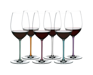 6 red wine filled RIEDEL Fatto A Mano Cabernet/Merlot glasses with stems which are colored in mint, orange, mauve, white, turquoise and violet stand slightly offset side by side.