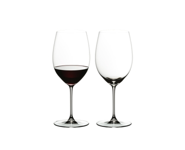 Two glasses RIEDEL Veritas Cabernet/Merlot on a white background. The glass on the left side is filled with red wine, the other one is unfilled.