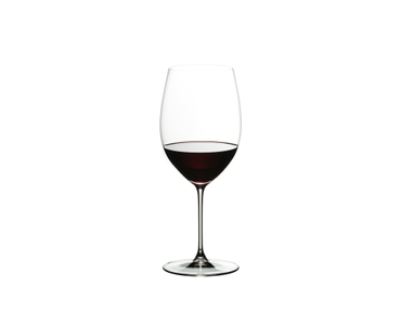 A woman sits on an armchair and looks at the red wine in the RIEDEL Veritas Cabernet/Merlot glass she holds in her hand.