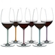 6 red wine filled RIEDEL Fatto A Mano Cabernet/Merlot glasses with stems which are colored in mint, orange, mauve, white, turquoise and violet stand slightly offset side by side.