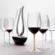 6 red wine filled RIEDEL Fatto A Mano Cabernet/Merlot glasses with stems which are colored in mint, orange, mauve, white, turquoise and violet stand slightly offset side by side on white background.