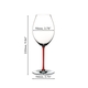 A red wine filled RIEDEL Fatto A Mano Syrah red glass with a red stem on a white background.