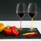 Two red wine filled RIEDEL Fatto A Mano Syrah glasses with a red and a yellow stem on a slate plate with stuffed peppers.