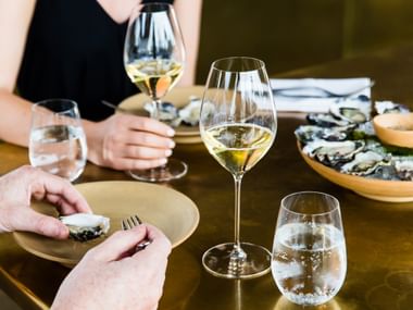 Two RIEDEL Veritas Champagne glasses on a table setting filled with champagne next to oysters.