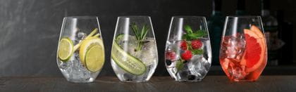 SPIEGELAU Gin und Tonic Gläser auf einem hölzernen Sideboard, jedes davon gefüllt mit einem anderen Gin Cocktail.<br/>