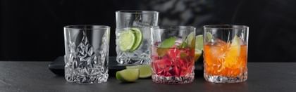 Quatre verres à whisky NACHTMANN Sculpture sur une table, trois d'entre eux étant remplis de différentes boissons alcoolisées et non alcoolisées. Entre les verres, la table est décorée de tranches de citron vert.<br/>