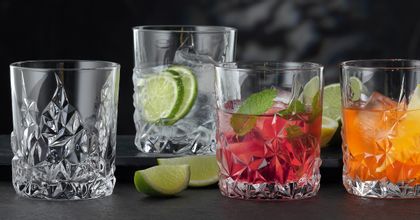 Four NACHTMANN Sculpture Whiskey tumblers on a table, three of them filled with different alcoholic and non-alcoholic drinks. Inbetween the glasses the table is decorated with slices of lime.<br/>