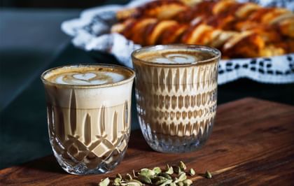 The NACHTMANN Barista Ethno and Noblesse Cappuccino/Flat White glass filled with coffee with pastries in the backdrop