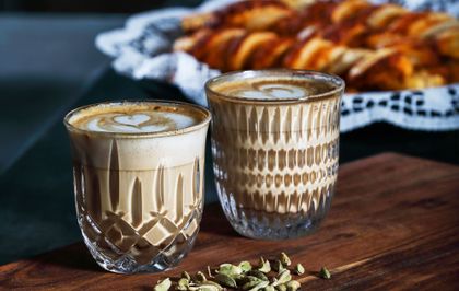 The NACHTMANN Barista Ethno and Noblesse Cappuccino/Flat White glass filled with coffee with pastries in the backdrop.