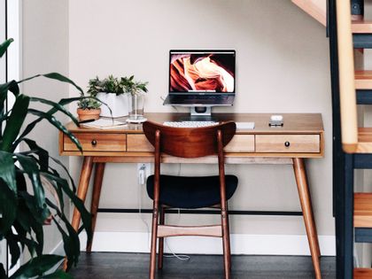 A wooden table with a computer and plants is placed on top.