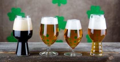 several Beer glasses filld with several beer an a table with fourclover as decoration