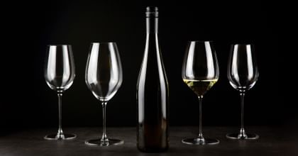four wine glasses with bottle in between and black background