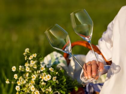 a woman is holding two empty champagne wine glasses, and stands in a meadow with flowers