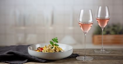 two glasses of rose next to noodle dish