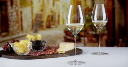 two white wine glasses in front of cheese plate