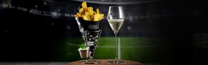 RIEDEL wine glass next to a bag of crisps with a soccer stadium background