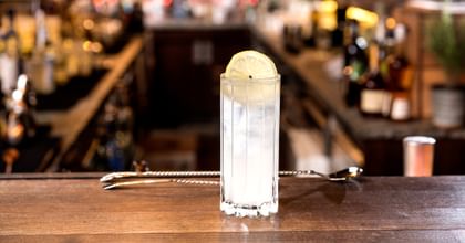 Highball glass filled with a cocktail, a bar in the background
