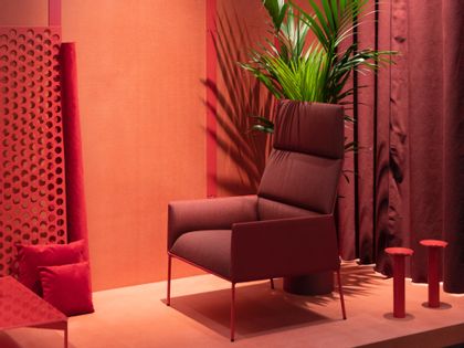 A pink room with a pink chair with a tall plant placed behind the chair.