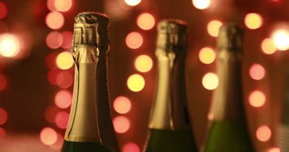 The top of three Champagne bottles with fairy lights in the background.