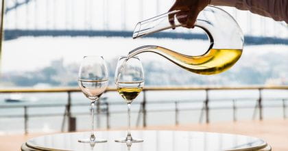 Hand pouring white wine from the RIEDEL Amadeo Decanter into two RIEDEL Veritas Riesling glasses.