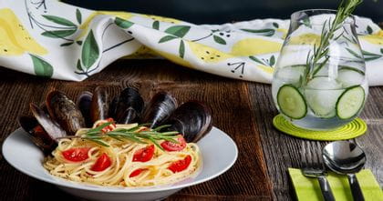 RIEDEL Gin Set Classic glass filled with gin & tonic on a table top next to a bowl of gin & lemon pasta with mussels.