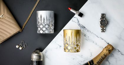 RIEDEL Laudon Silver and Gold on a black and white marble background with jewellery, makeup and a purse scattered around them.
