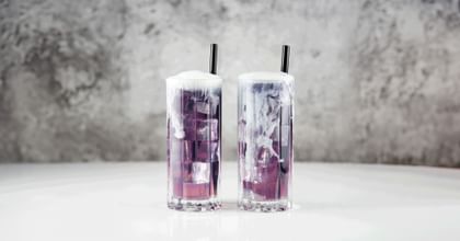 two RIEDEL Drink Specific Glassware Highball Glasses with a pink/blue cocktail in it