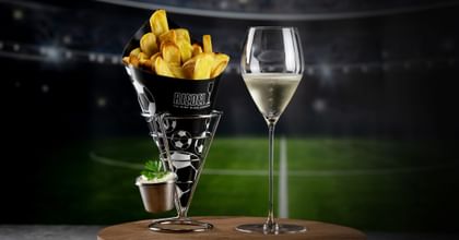 RIEDEL wine glass next to a bag of french fries with a football field in the background