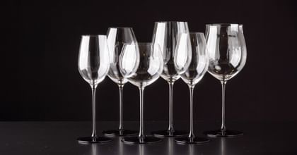 various RIEDEL wine glasses lined up against black background