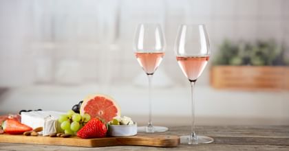 two rose glasses next to food platter