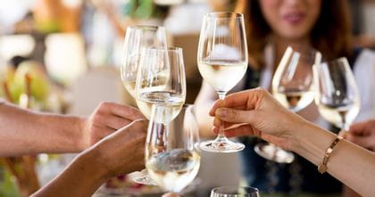 People cheersing with wine glasses filled with white wine.