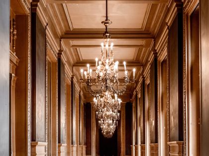 A large gold crystal chandelier hanging from a large hallway.