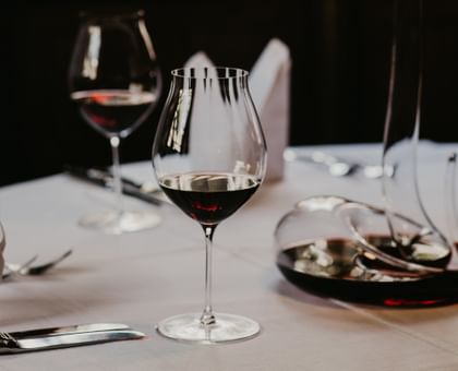 RIEDEL Performance Pinot Noir table on white table with Mamba decanter filled with red wine.
