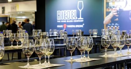 Good Food Wine Show RIEDEL Sensory Tasting setup. Rows of the RIEDEL Ouverture Magnum glasses filled with wines on top of a table and tasting mat. The RIEDEL Logo is in the background on a media wall.