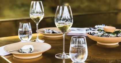 Two RIEDEL Veritas Champagne glasses filled with Champagne on a bronze table top next to a water glass and two ceramic plates.