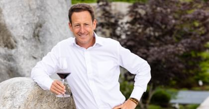 Maximilian J. Riedel holding a glass of red wine and smiling