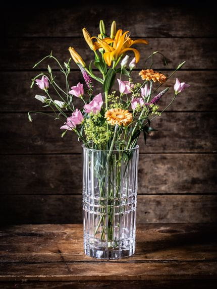 The crystal NACHTMANN vase Square, filled with orange and pink flowers, on a dark wooden sideboard.<br/>