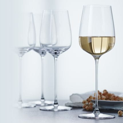 Vier SPIEGELAU Willsberger Anniversary Weißweingläser, eines davon mit Weißwein gefüllt.<br/>